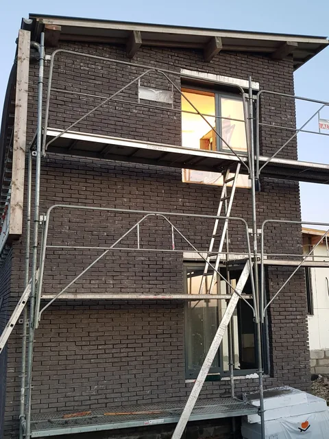 Façade en brique sombre d’une construction neuve, montée sous échafaudage