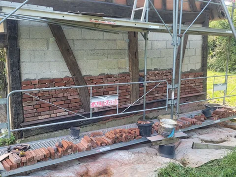 Mur à colombages dont les panneaux sont repris en brique rouge, sous échafaudage