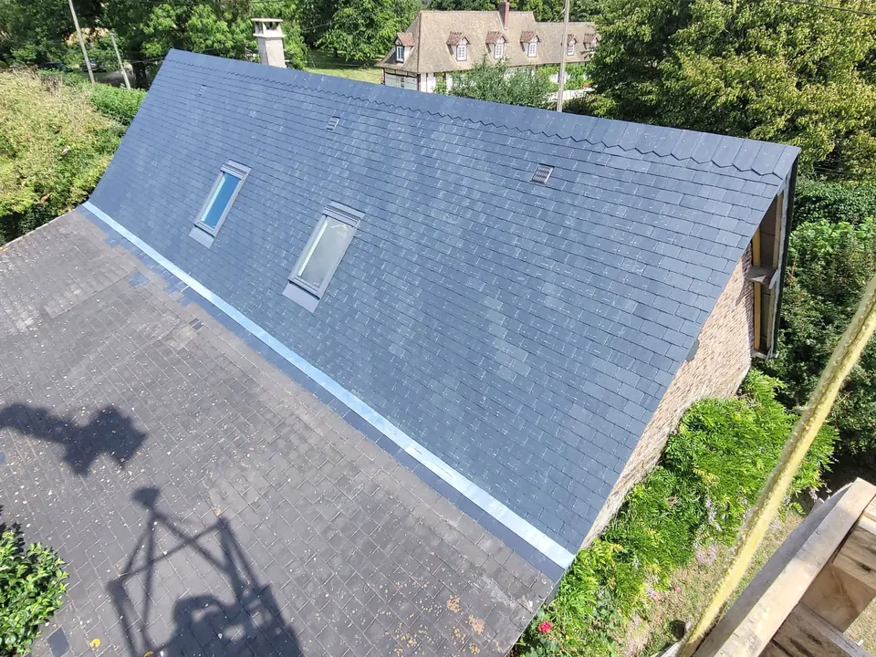 Vue plongeante sur un long pan de toiture en ardoise neuve percé de deux fenêtres de toit