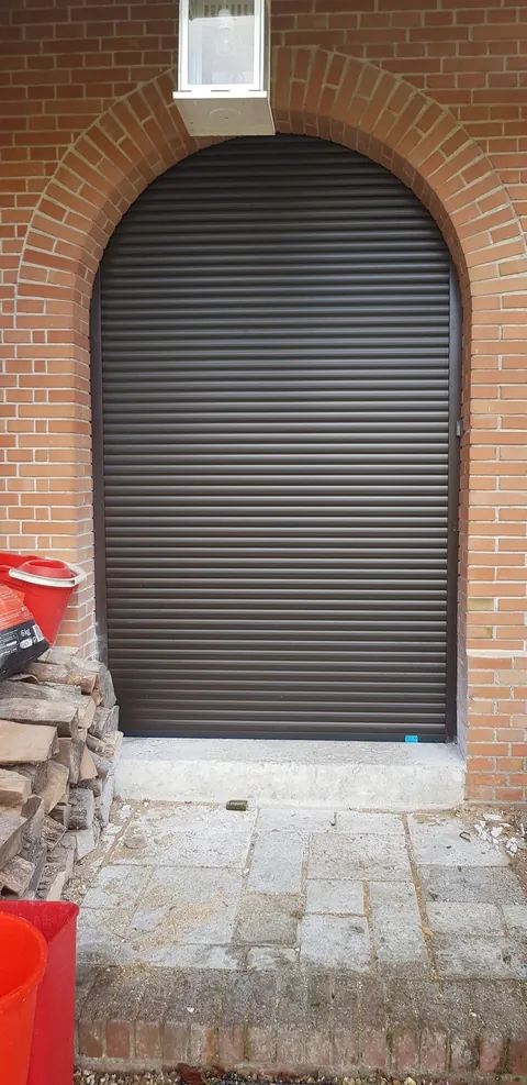 Volet roulant brun posé au-dessus d’une porte cintrée dans un mur de brique rouge